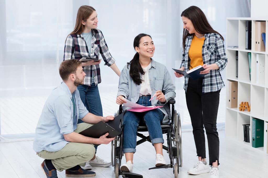 A diverse group of people surrounds a woman in a wheelchair, highlighting the importance of support in assistance daily living NDIS activities.