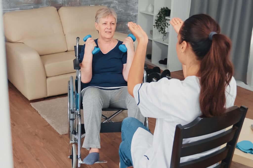 A nurse supports a woman in a wheelchair as she engages in personal activities through tailored exercises.