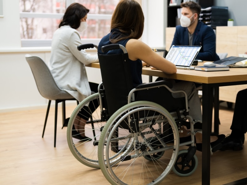 NDIS support coordination funding meeting, showcasing a person in a wheelchair collaborating with professionals in an office.