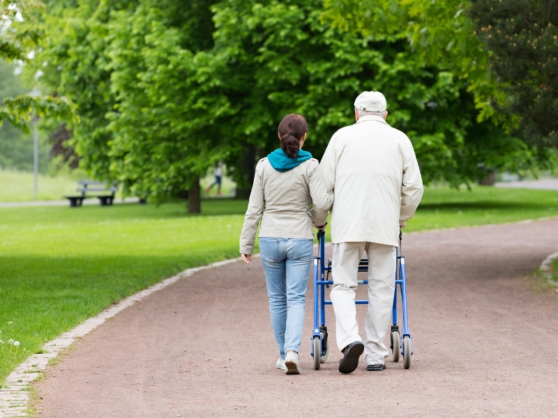 Elderly man with a walker supported by a caregiver in a park - disability help and support.