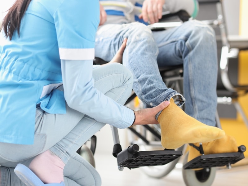 A healthcare worker providing assistance for people with disabilities, supporting a person's leg while in a wheelchair.