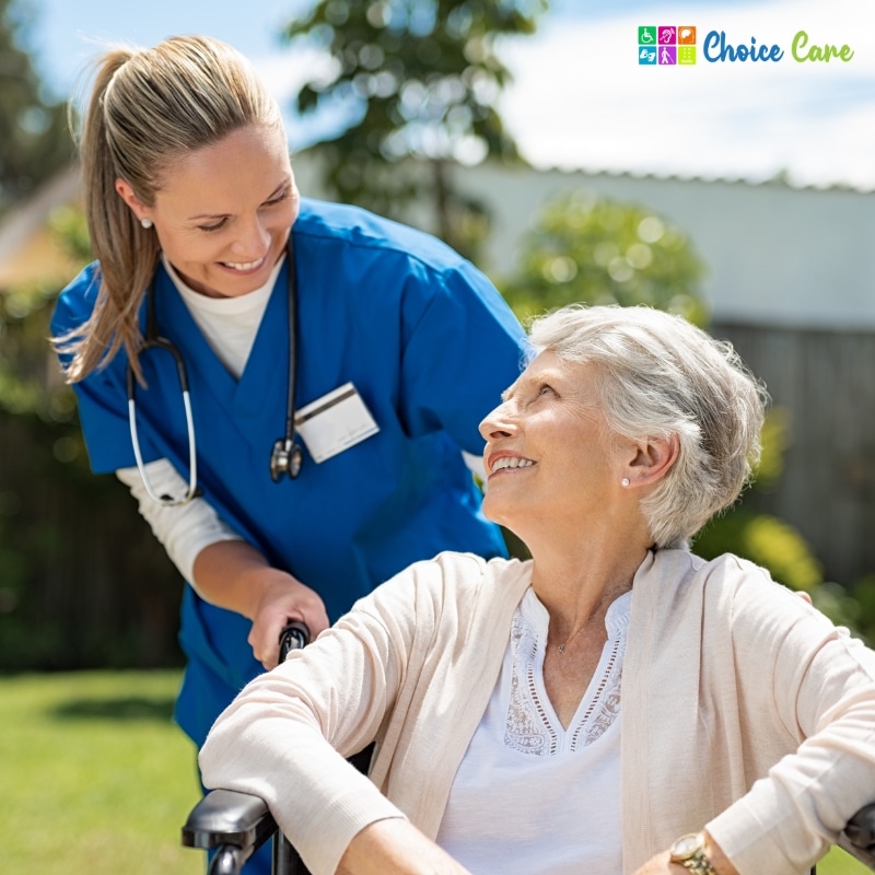 Smiling elderly woman in wheelchair assisted by NDIS provider Acacia Gardens nurse outdoors, showcasing compassionate disability support care.