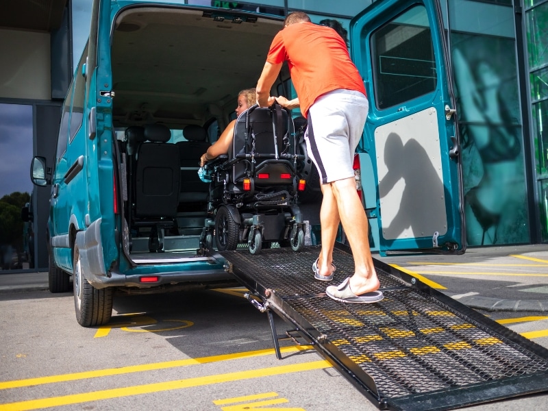 Person assisting wheelchair user into a van with a ramp - NDIS personal activities support for transportation.