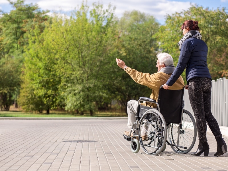 Elderly man in a wheelchair outdoors with a caregiver - NDIS personal activities funding for outdoor social engagement.