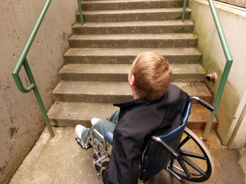 A person in a wheelchair facing stairs, highlighting challenges in finding accessible housing.