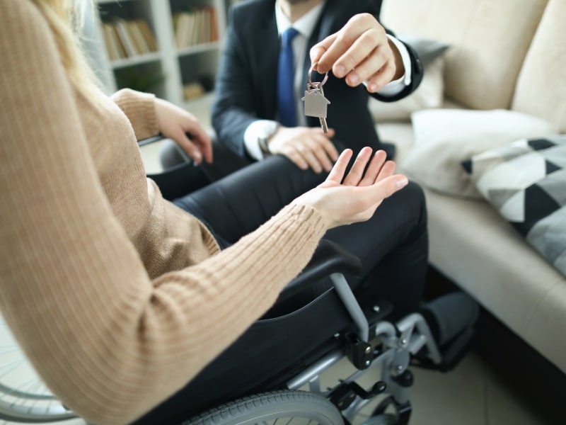 A person in a wheelchair receiving house keys, symbolizing success in finding accessible housing.