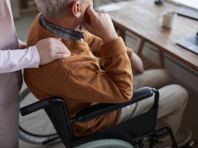 Elderly man in a wheelchair, comforted by a caregiver, emphasizing emotional support provided through personalised care plans.