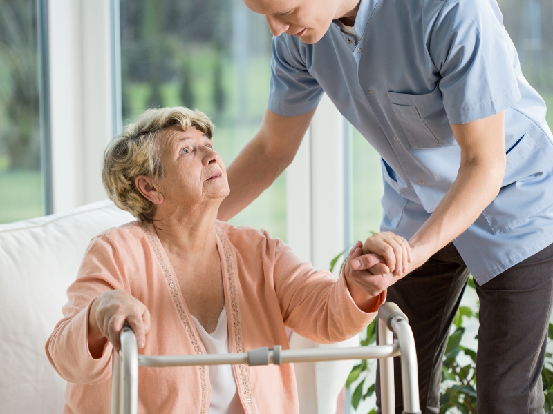 Elderly woman using a walker, assisted by a caregiver, illustrating the benefits of personalised care plans in daily support.