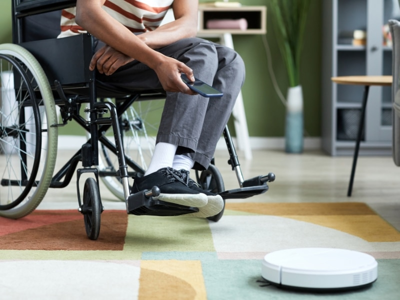 A person using a robotic vacuum promotes independence and disability by making household chores easier and more manageable.