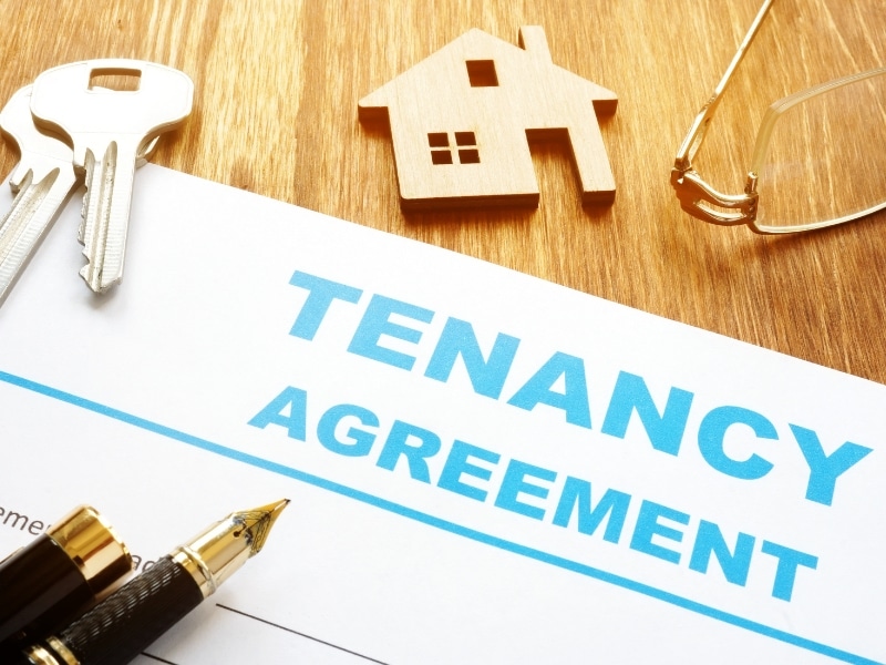 A tenancy agreement document, keys, a house model, and a pen on a table. Supported tenancy helps people with disabilities find housing.