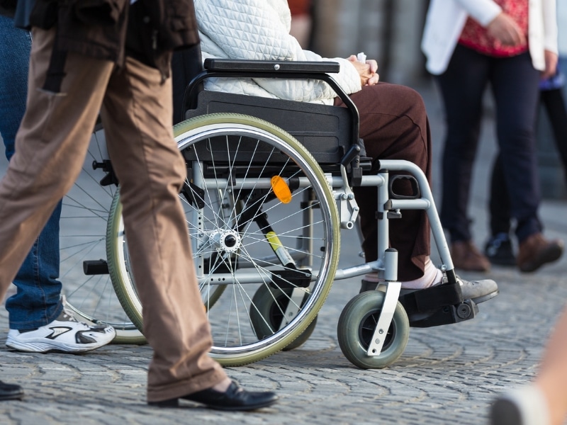 Person in a wheelchair being assisted on a paved street, highlighting everyday transportation options for disabled individuals.