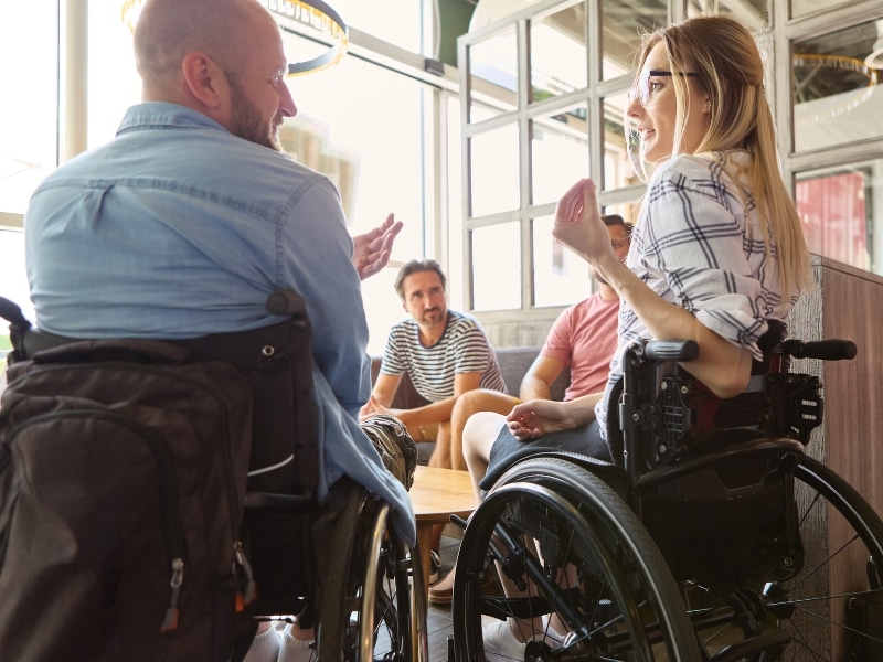 A social gathering featuring individuals in wheelchairs enjoying daily life assistance, fostering inclusion and community engagement.