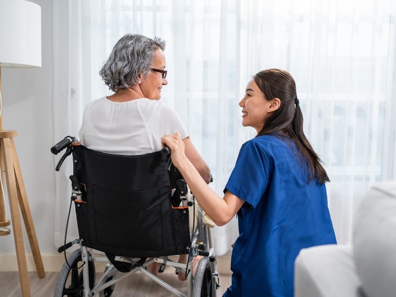 Person in a wheelchair receiving assistance with daily personal activities, ensuring comfort and support.