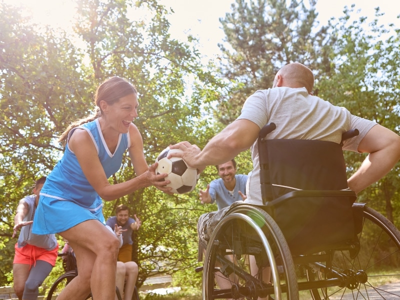 A social gathering featuring people in wheelchairs playing ball, highlighting inclusive daily life assistance and community engagement.