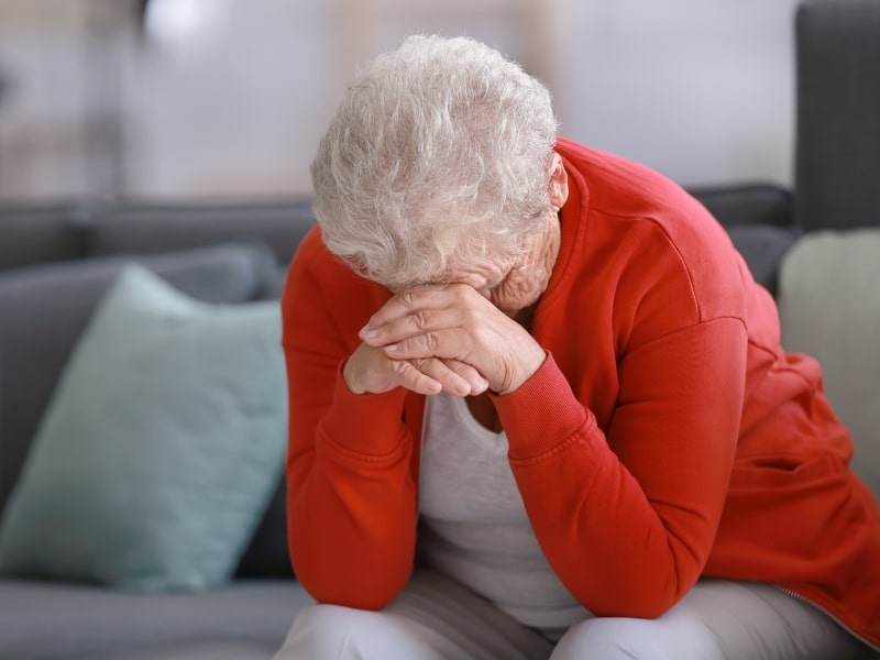 Elderly woman sitting with head in hands, overwhelmed by limited funding for disability services and emotional stress.