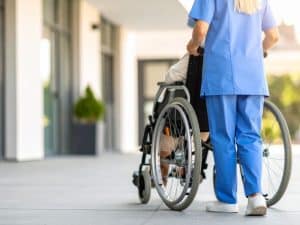 Support for special needs involving a nurse pushing a wheelchair outside a modern care facility