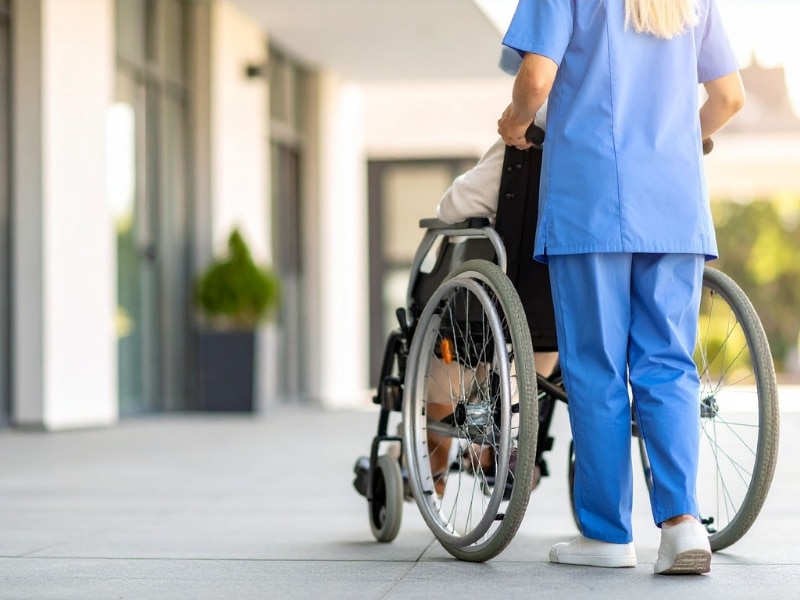 Support for special needs involving a nurse pushing a wheelchair outside a modern care facility